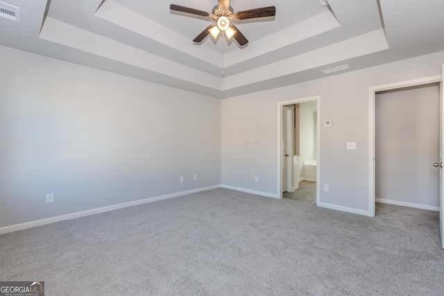 unfurnished bedroom with a tray ceiling, ensuite bath, and ceiling fan