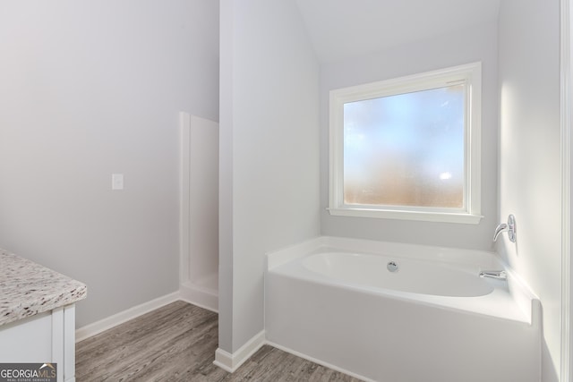 bathroom with a washtub, wood-type flooring, vanity, and vaulted ceiling