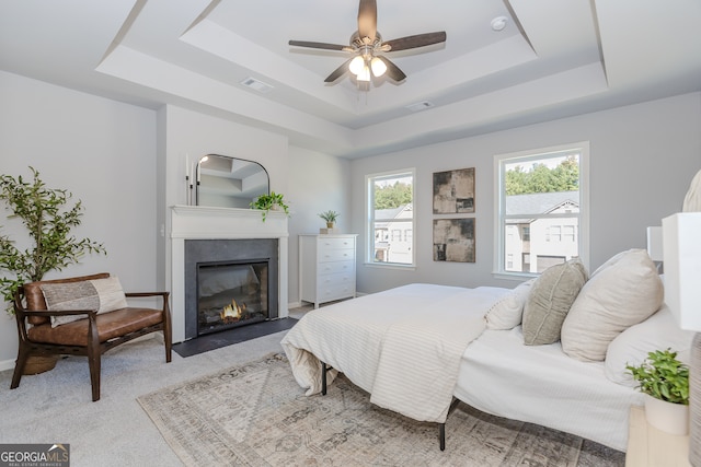 bedroom with a tray ceiling, a fireplace with flush hearth, visible vents, and light colored carpet