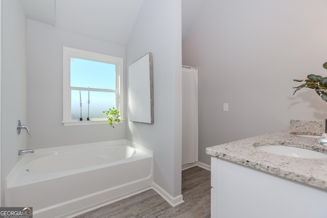 bathroom featuring a garden tub, a sink, baseboards, and wood finished floors