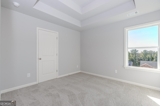 carpeted empty room featuring a raised ceiling, visible vents, and baseboards