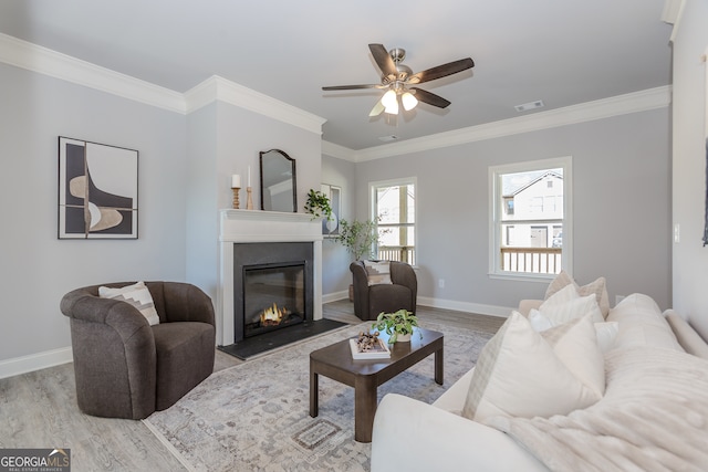 living room with a glass covered fireplace, wood finished floors, visible vents, and crown molding