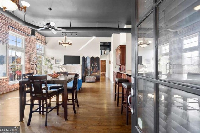 dining room with ceiling fan with notable chandelier, a healthy amount of sunlight, brick wall, and hardwood / wood-style floors