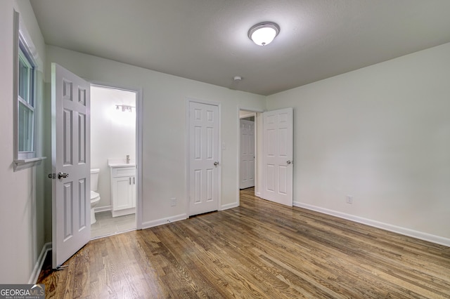 unfurnished bedroom featuring ensuite bath, a closet, and hardwood / wood-style flooring