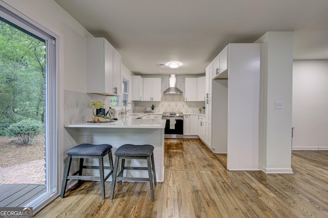 kitchen with white cabinets, wall chimney range hood, decorative backsplash, stainless steel range oven, and kitchen peninsula