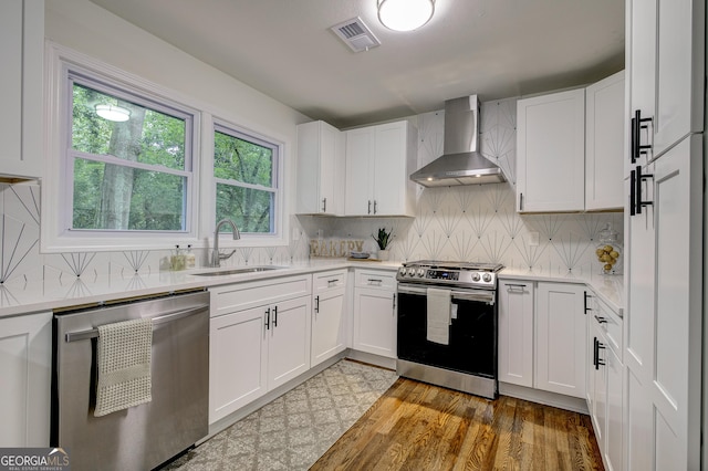 kitchen with backsplash, white cabinets, wall chimney range hood, sink, and appliances with stainless steel finishes