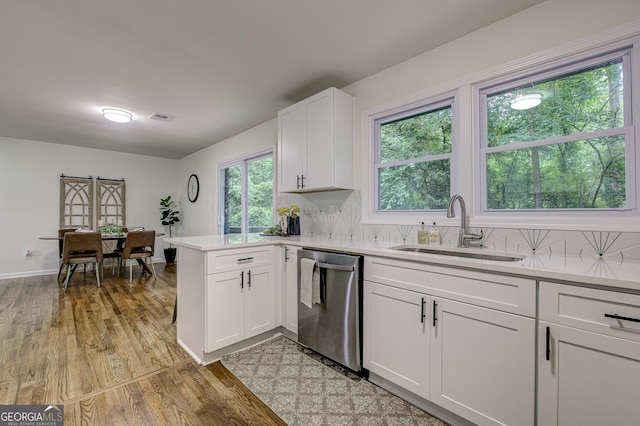 kitchen featuring kitchen peninsula, backsplash, sink, dishwasher, and white cabinetry