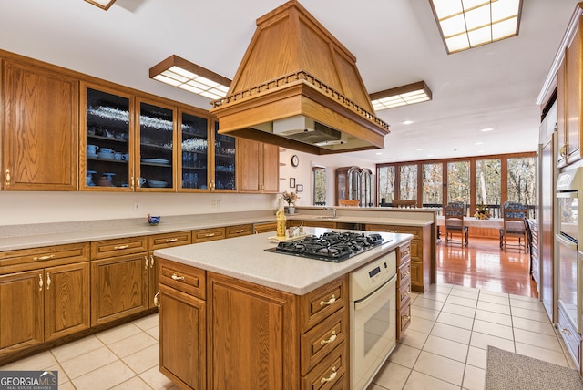 kitchen with stainless steel gas cooktop, a kitchen island, kitchen peninsula, oven, and light tile patterned floors