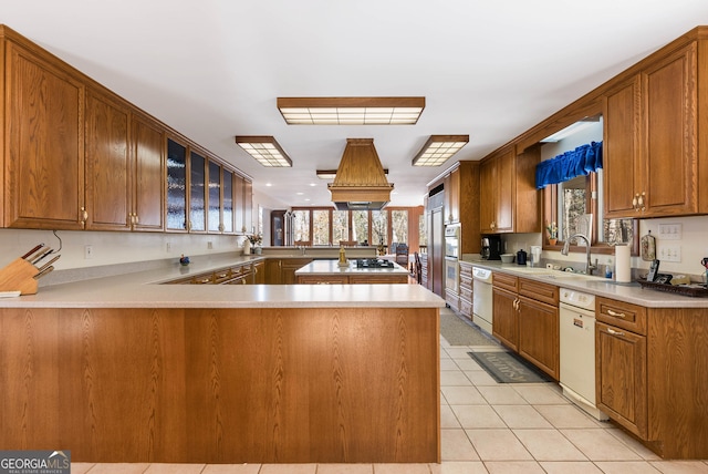 kitchen featuring white dishwasher, kitchen peninsula, sink, light tile patterned flooring, and stainless steel double oven