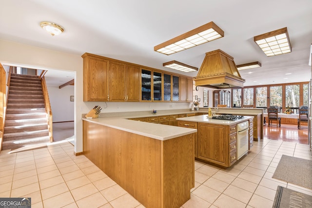 kitchen with light tile patterned floors, kitchen peninsula, premium range hood, and stainless steel gas cooktop