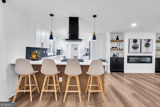 kitchen featuring island exhaust hood, kitchen peninsula, stainless steel gas cooktop, sink, and white cabinetry