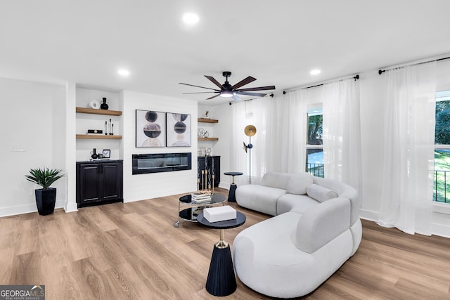 living room with ceiling fan, a large fireplace, light wood-type flooring, and a wealth of natural light