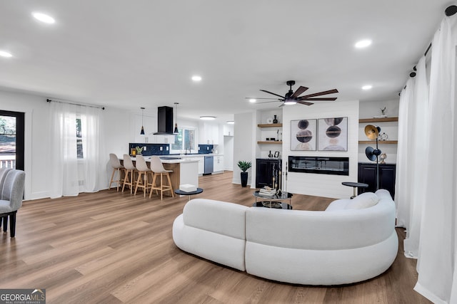 living room with a large fireplace, light hardwood / wood-style floors, ceiling fan, and sink