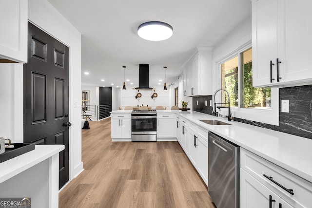 kitchen with kitchen peninsula, appliances with stainless steel finishes, island exhaust hood, sink, and decorative light fixtures