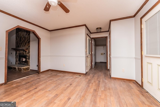 spare room featuring ceiling fan, a fireplace, ornamental molding, and light wood-type flooring