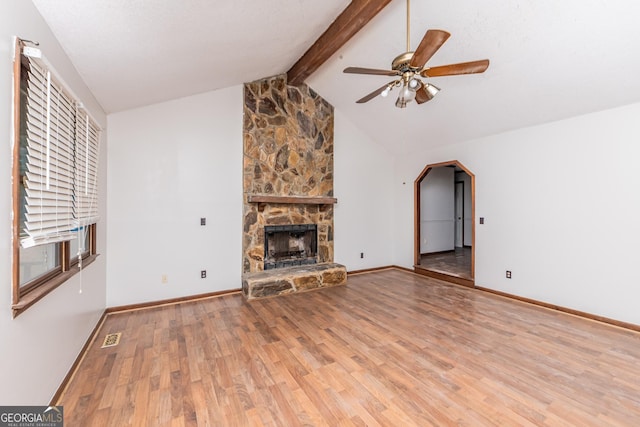 unfurnished living room featuring vaulted ceiling with beams, ceiling fan, a stone fireplace, and light wood-type flooring