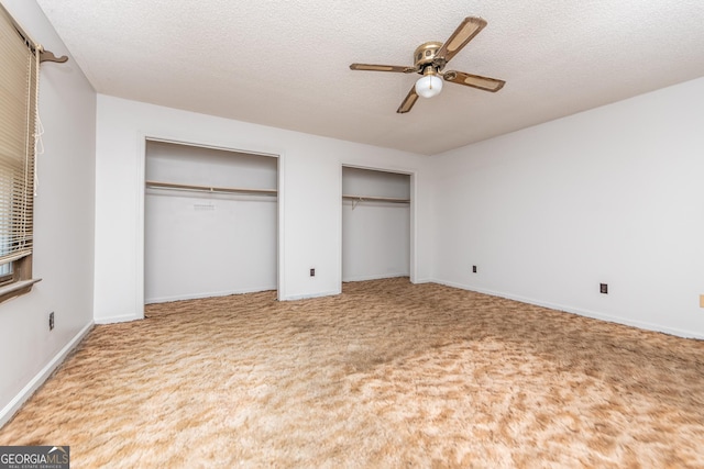 unfurnished bedroom featuring carpet flooring, a textured ceiling, two closets, and ceiling fan