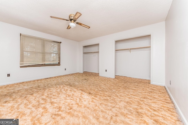 unfurnished bedroom featuring two closets, a textured ceiling, light colored carpet, and ceiling fan