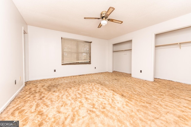 unfurnished bedroom with ceiling fan, carpet floors, a textured ceiling, and two closets