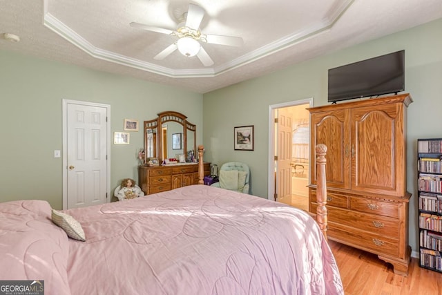 bedroom featuring a tray ceiling, connected bathroom, ceiling fan, and light wood-type flooring