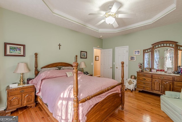 bedroom with a textured ceiling, a tray ceiling, light hardwood / wood-style flooring, and ceiling fan