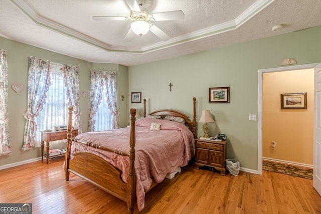 bedroom with crown molding, ceiling fan, a textured ceiling, a tray ceiling, and light hardwood / wood-style floors