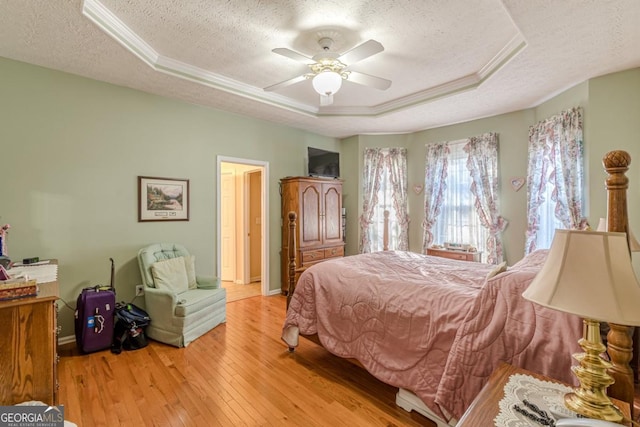 bedroom featuring ceiling fan, a raised ceiling, light wood-type flooring, and a textured ceiling