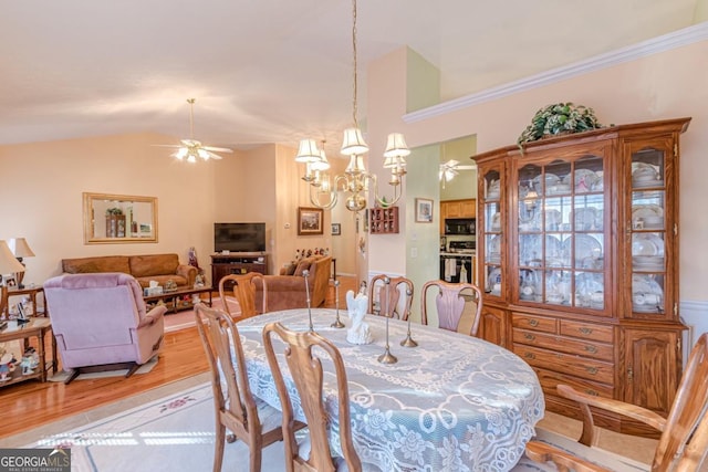 dining room with vaulted ceiling, ceiling fan with notable chandelier, and light wood-type flooring