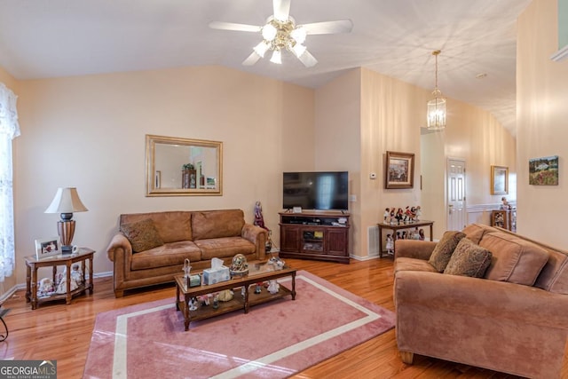 living room with ceiling fan with notable chandelier, light hardwood / wood-style flooring, and vaulted ceiling