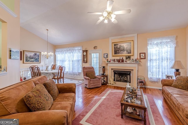 living room with a healthy amount of sunlight, high vaulted ceiling, wood-type flooring, and ceiling fan with notable chandelier