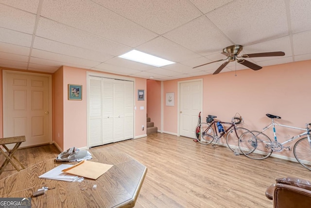 exercise area featuring a paneled ceiling, ceiling fan, and light wood-type flooring