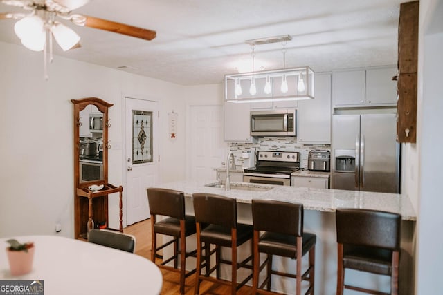 kitchen featuring decorative backsplash, appliances with stainless steel finishes, a breakfast bar, sink, and light hardwood / wood-style flooring