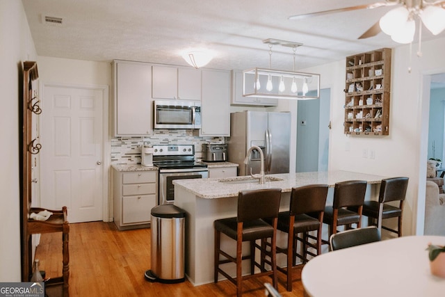 kitchen featuring sink, light wood-type flooring, decorative light fixtures, a kitchen bar, and stainless steel appliances