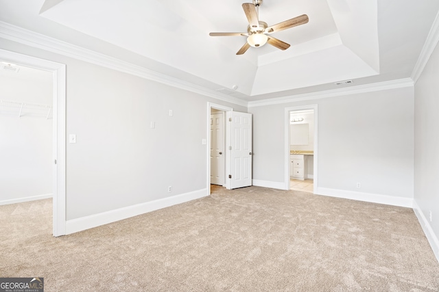 unfurnished bedroom featuring light carpet, a raised ceiling, a walk in closet, ceiling fan, and ornamental molding