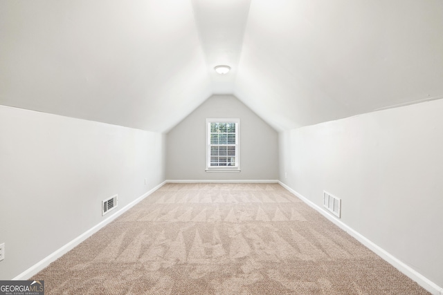 additional living space featuring light colored carpet and vaulted ceiling