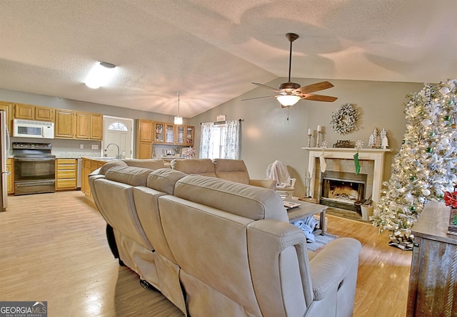 living room featuring lofted ceiling, ceiling fan, light wood-type flooring, a textured ceiling, and a fireplace