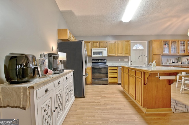 kitchen with a kitchen bar, appliances with stainless steel finishes, sink, light hardwood / wood-style flooring, and an island with sink