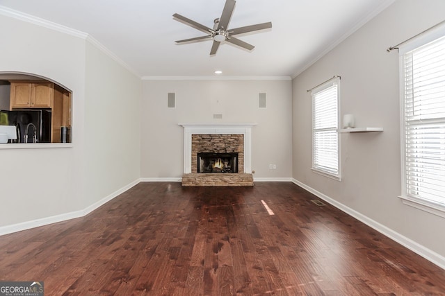 unfurnished living room with ornamental molding, a stone fireplace, ceiling fan, and dark wood-type flooring