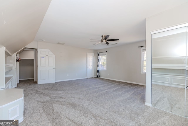 unfurnished bedroom with ceiling fan, lofted ceiling, light colored carpet, baseboards, and multiple closets