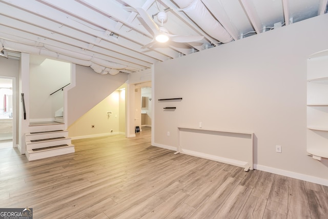 basement featuring baseboards, ceiling fan, light wood finished floors, and stairs