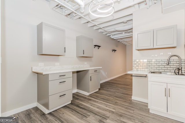 kitchen featuring baseboards, wood finished floors, light countertops, white cabinetry, and a sink