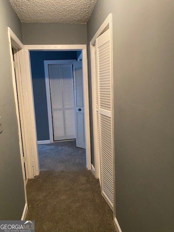 corridor with dark colored carpet and a textured ceiling