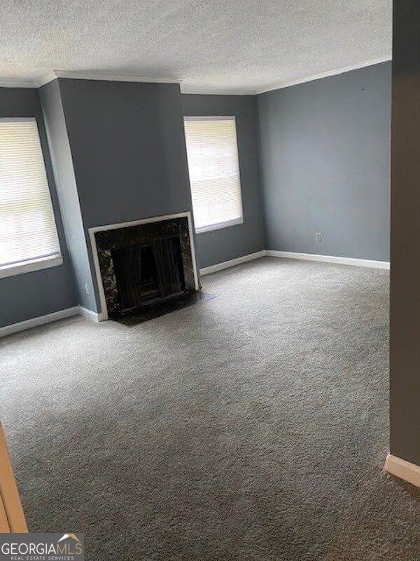 unfurnished living room with a textured ceiling, carpet floors, and crown molding