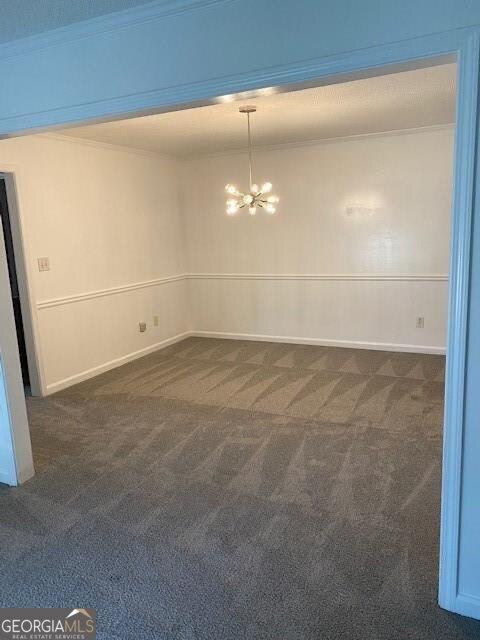 spare room featuring dark carpet, ornamental molding, and a chandelier