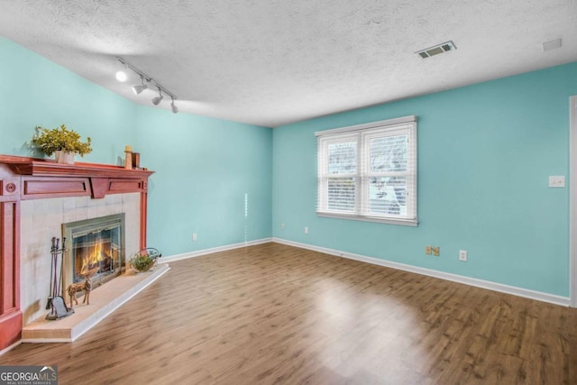 unfurnished living room featuring a tile fireplace, track lighting, a textured ceiling, and hardwood / wood-style flooring