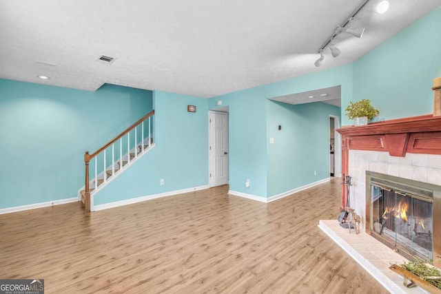 unfurnished living room with a fireplace, rail lighting, and wood-type flooring