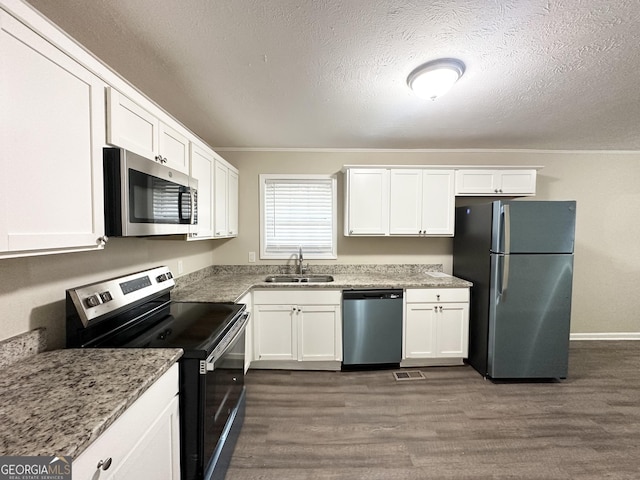 kitchen with light stone counters, stainless steel appliances, dark wood-type flooring, sink, and white cabinetry