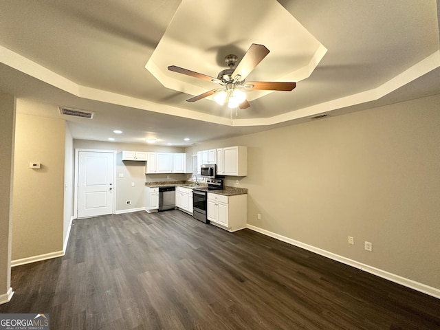 kitchen with white cabinetry, ceiling fan, stainless steel appliances, dark hardwood / wood-style flooring, and a tray ceiling