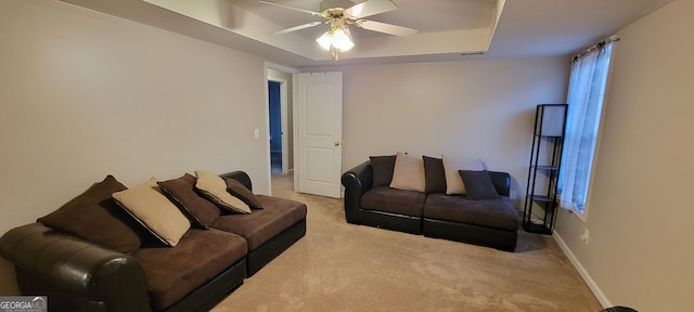 living room featuring light carpet, a tray ceiling, and ceiling fan