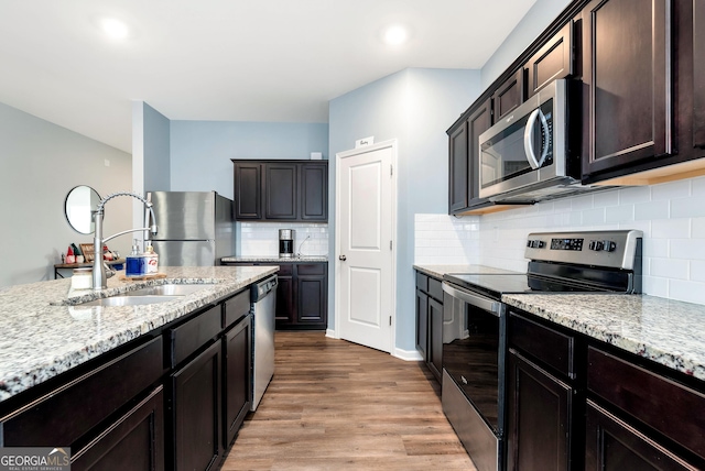 kitchen with a sink, backsplash, appliances with stainless steel finishes, light wood finished floors, and light stone countertops